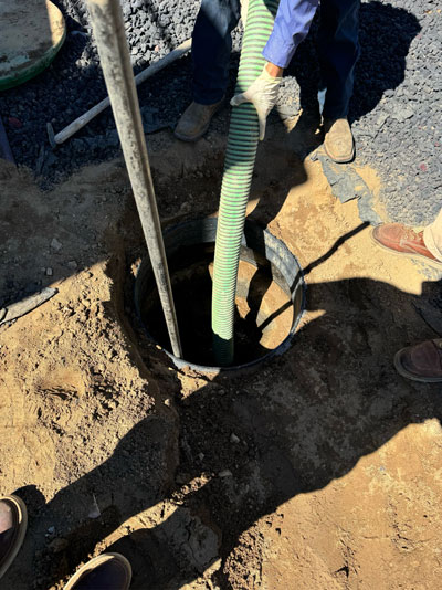 A septic tank being pumped out on a job site, with the suction hose lowered through the open tank lid into the ground