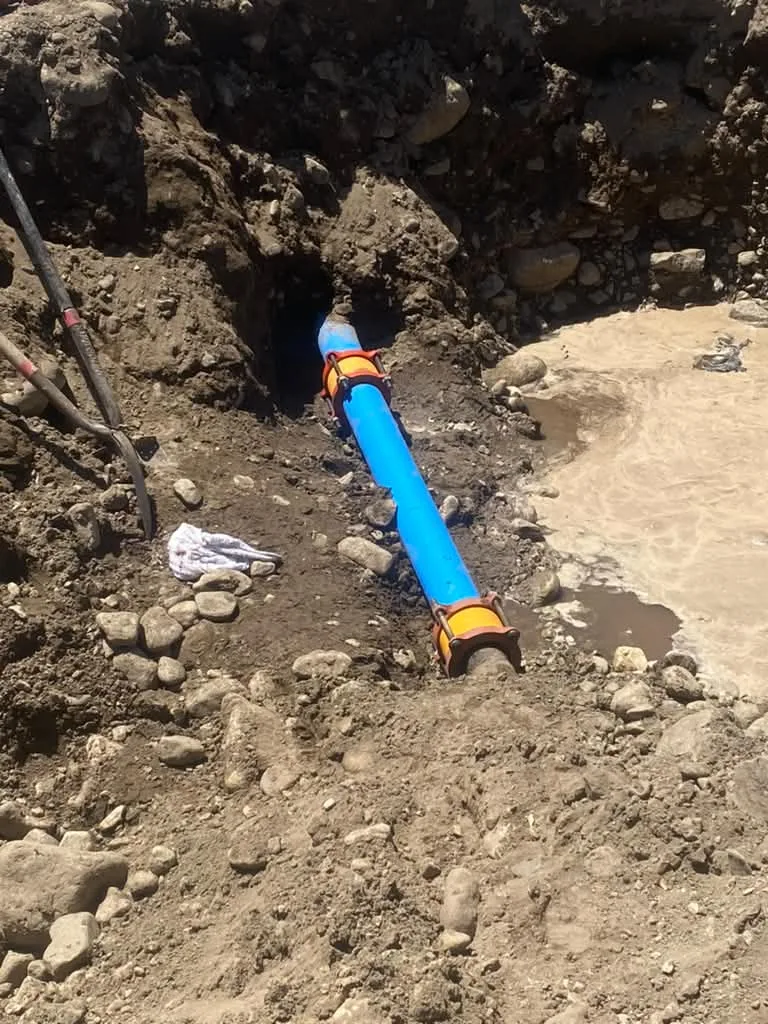 Blue poly water main laid in an open rocky trench with yellow fittings