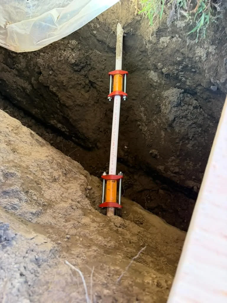 White cleanout riser with orange couplings standing in a fresh trench beside a driveway