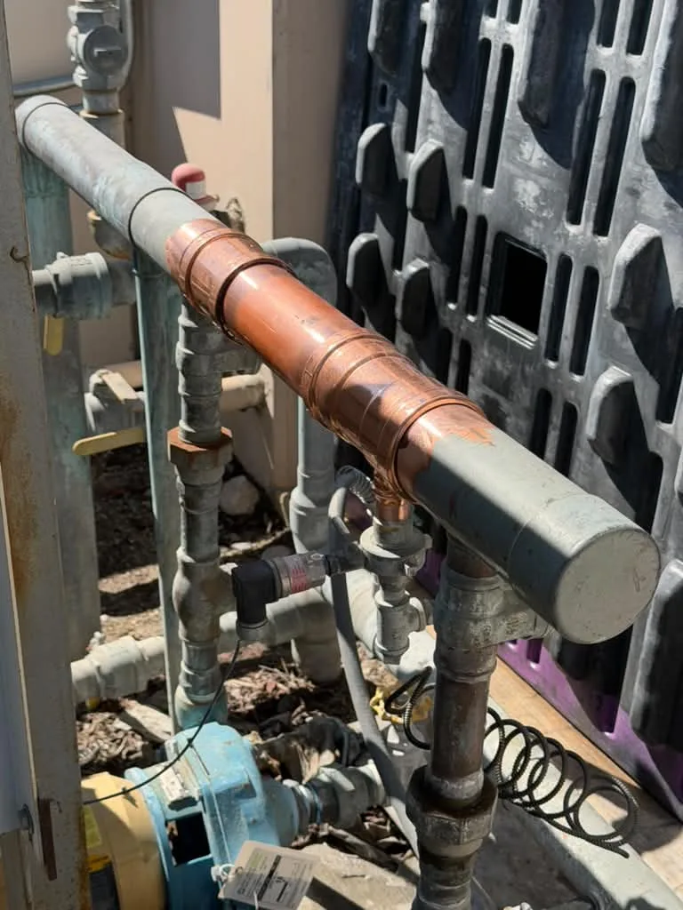 Overhead galvanized and copper manifold with backflow assembly against a louvered enclosure