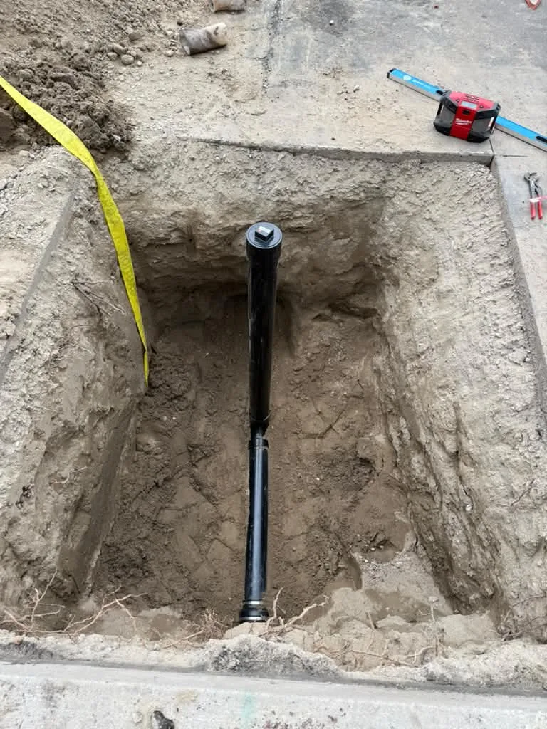 Black pipe riser standing in a saw-cut concrete opening with a level and tape measure