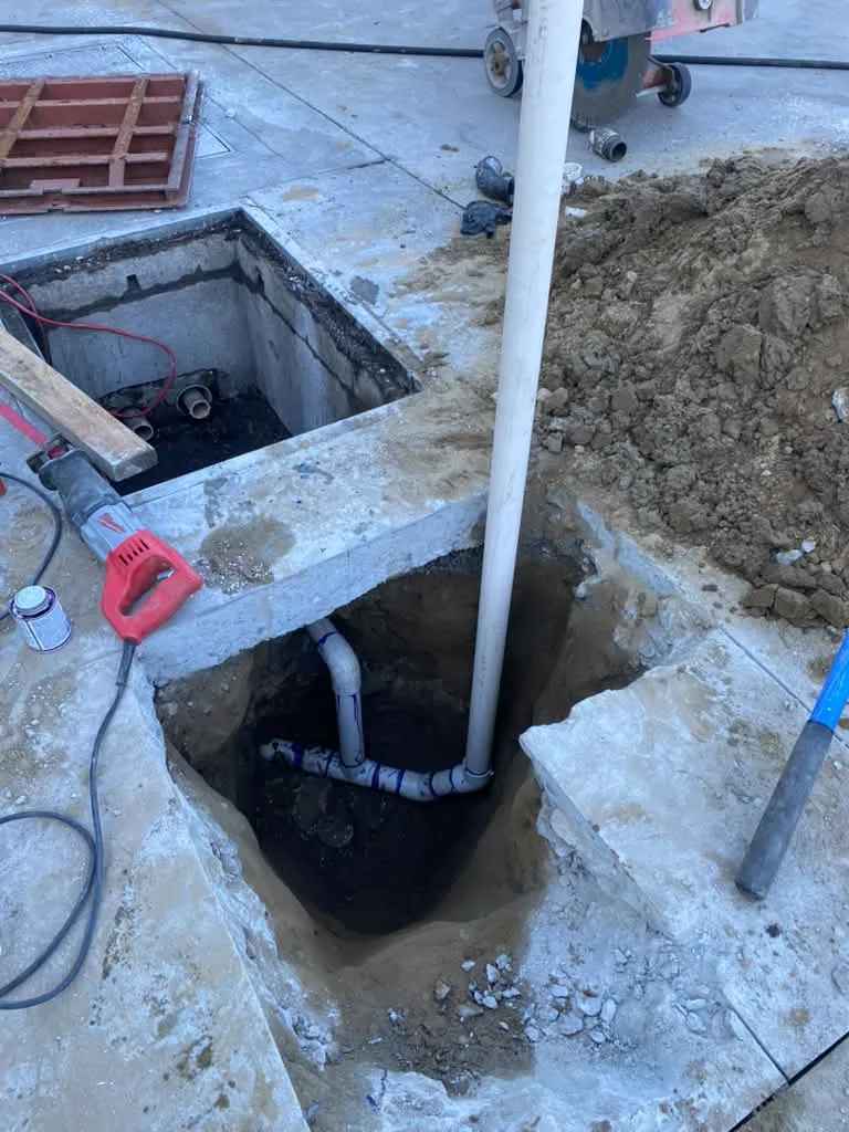 Saw-cut opening through a concrete slab exposing sewer pipe, pipe wrench and hose on deck