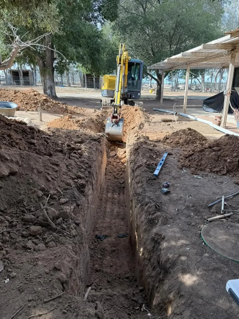 Long sewer trench under excavation with a mini excavator digging at the head of the cut