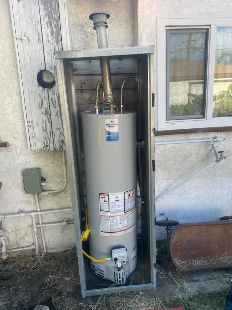 Newly installed exterior water heater in a steel enclosure against a house wall