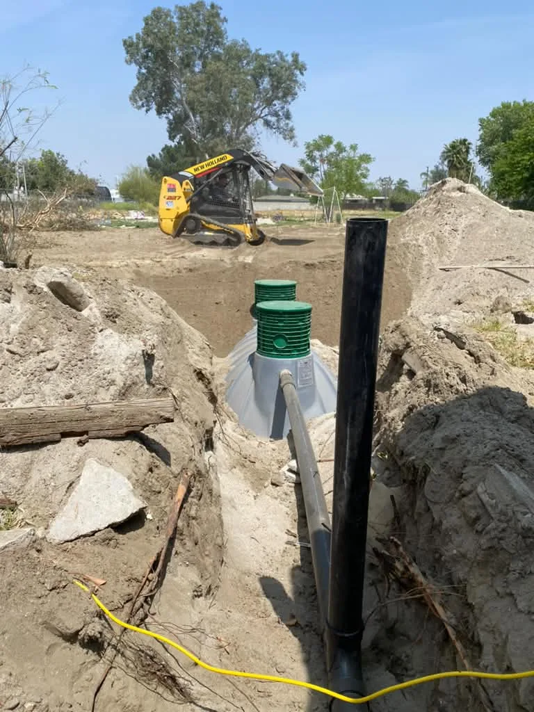 New septic tank with green risers set in an open trench, track loader working behind it