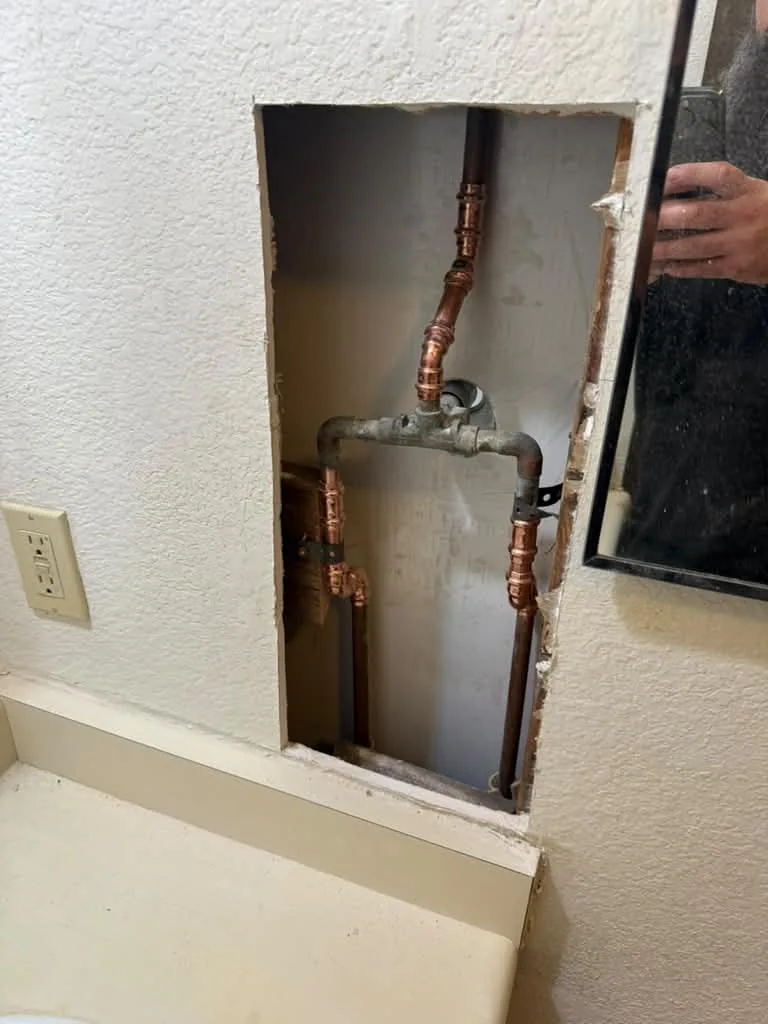 Drywall access cut exposing copper supply lines and shutoff valves