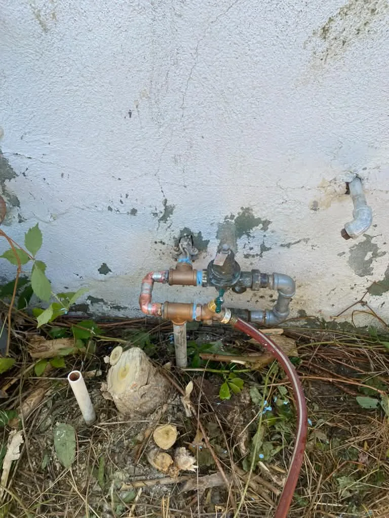 Brass shutoff valves and supply line exposed in a rocky yard excavation